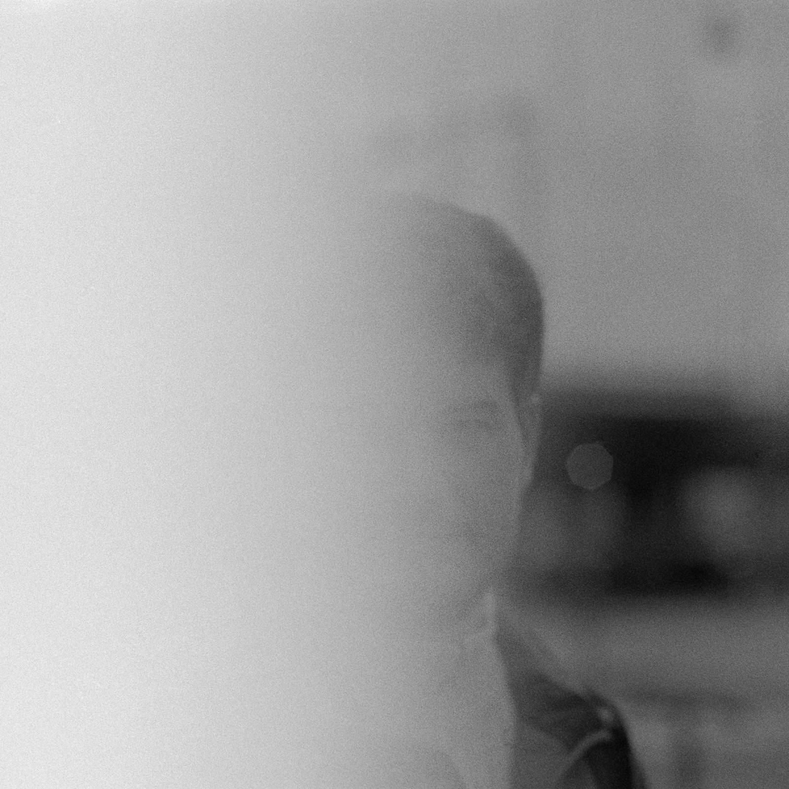 An out-of-focus black-and-white frame, mostly washed-out grey, with the blurred outline of a person’s head at the edge